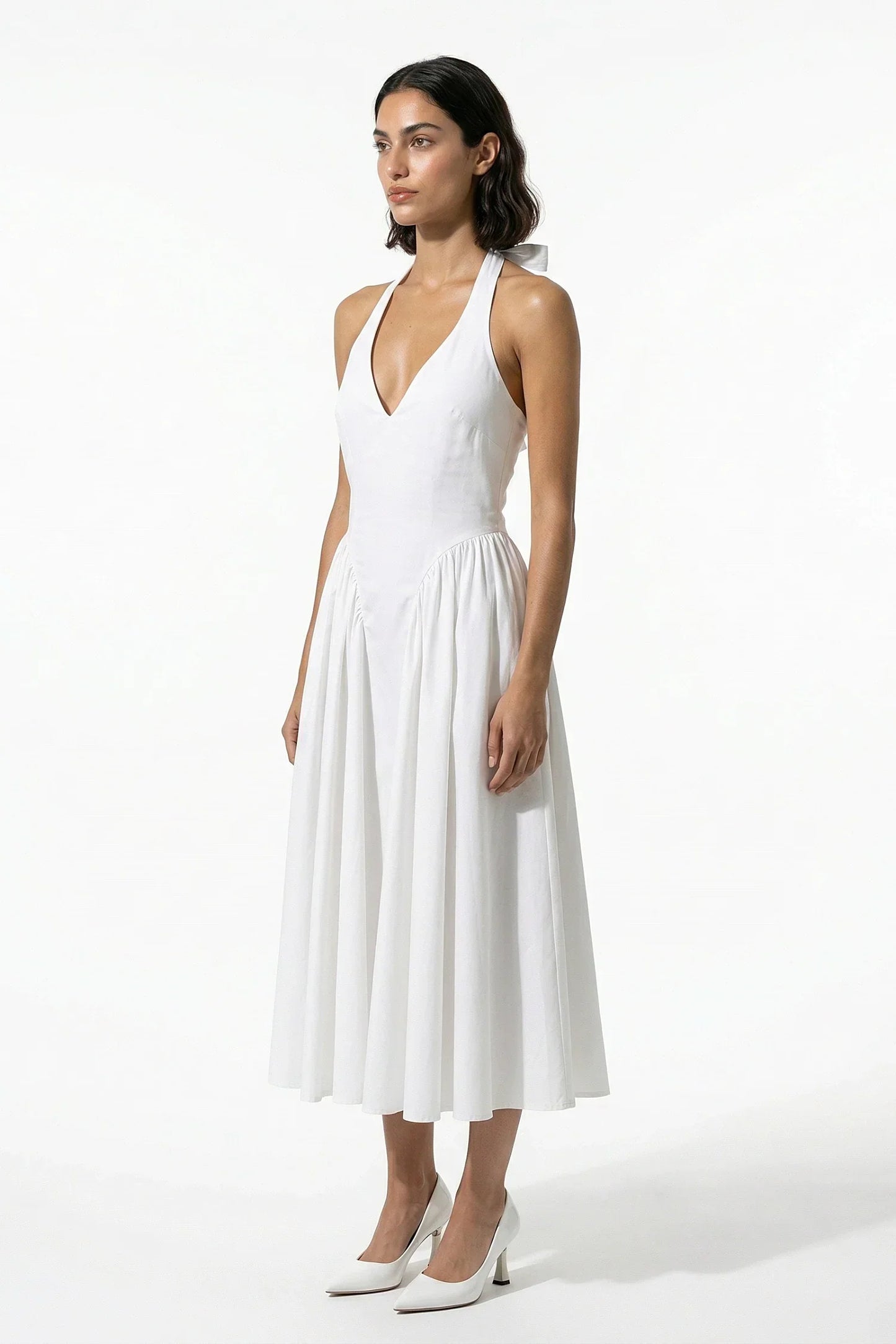 Side view of white halter midi dress with fitted waist and soft pleated skirt