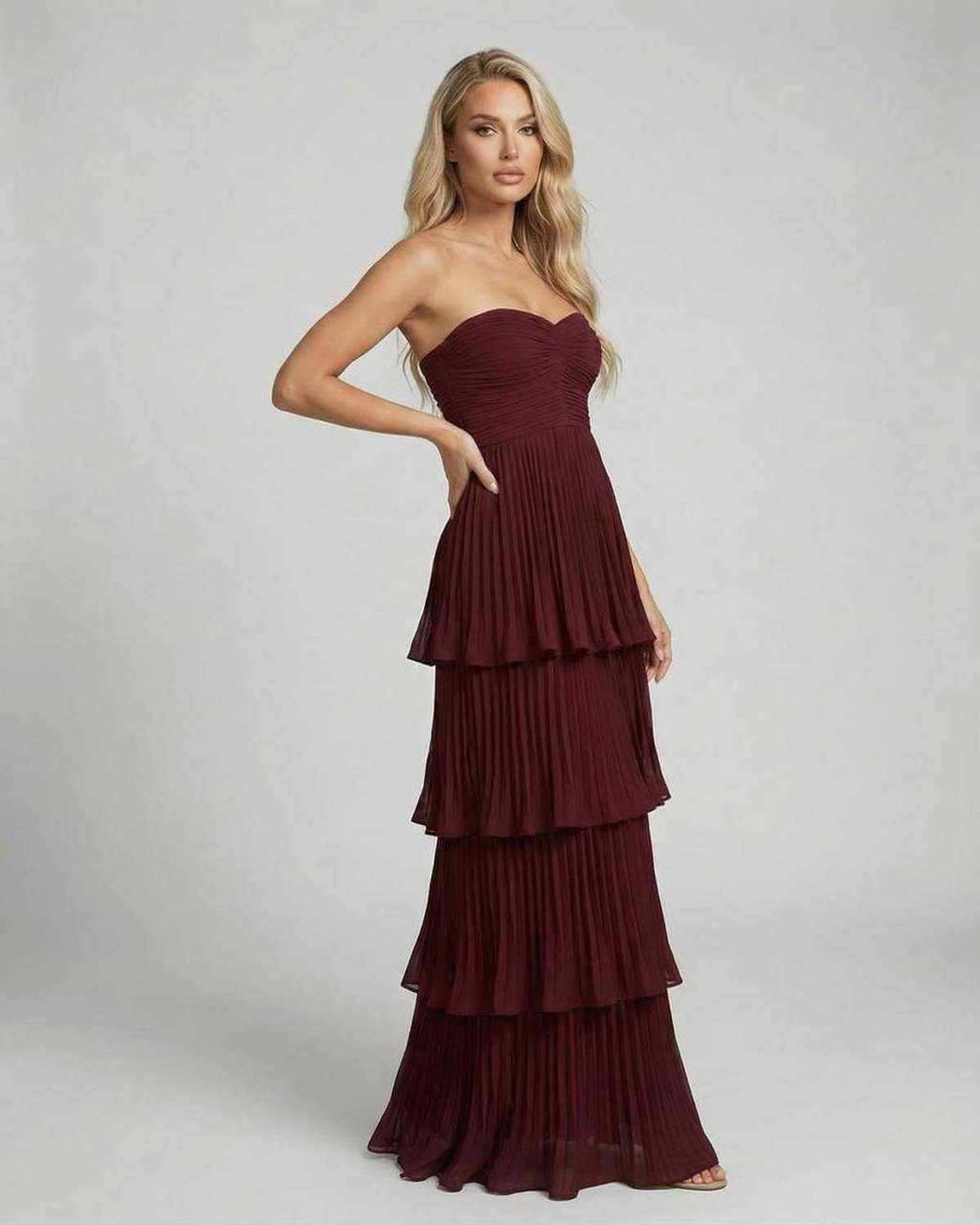 Side view of burgundy strapless maxi dress with pleated layers and flowy skirt