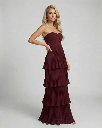 Side view of burgundy strapless maxi dress with pleated layers and flowy skirt