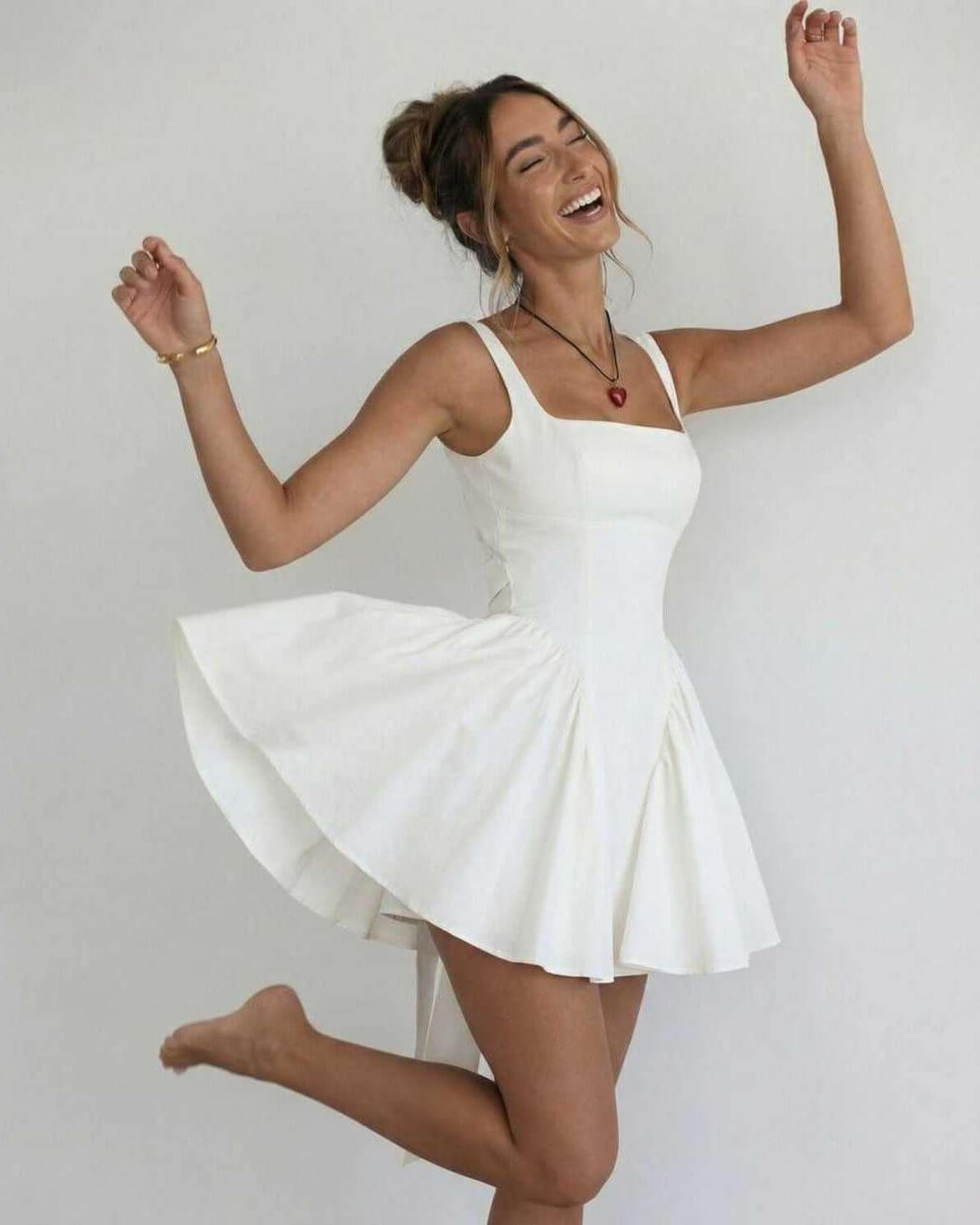Woman wearing white square neck mini dress twirling to show full flared skirt and open back